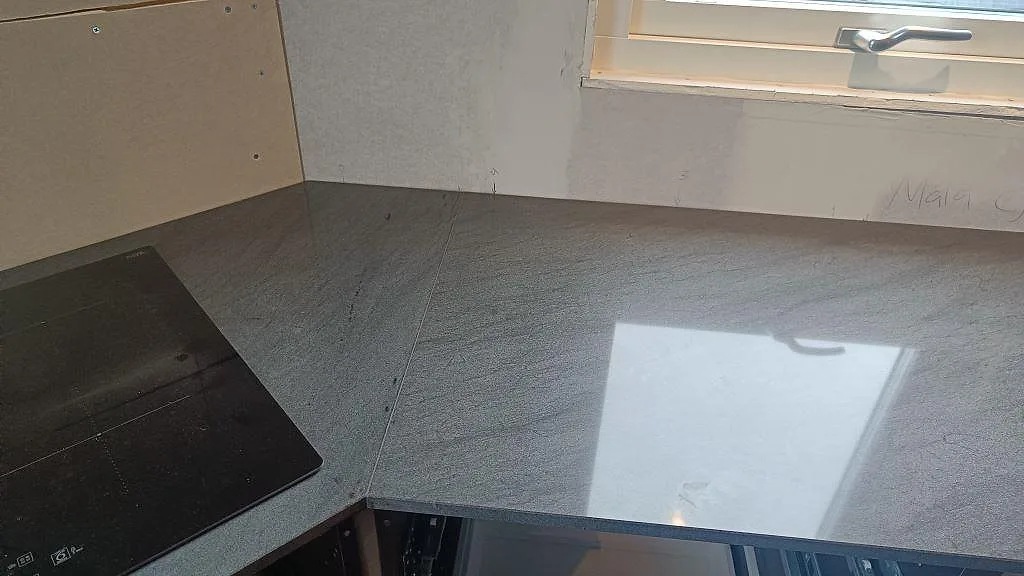 Polerad köksbänkskiva i Anthracite Elegante granit under fönster, med hällkant och ljusreflektion i Frillesås.