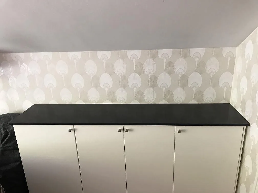 Bänkskiva i mörk antracitgrå Anthracite Elegante, polerad kvartskomposit, monterad på vita skåp mot mönstrad tapet i Helsingborg.