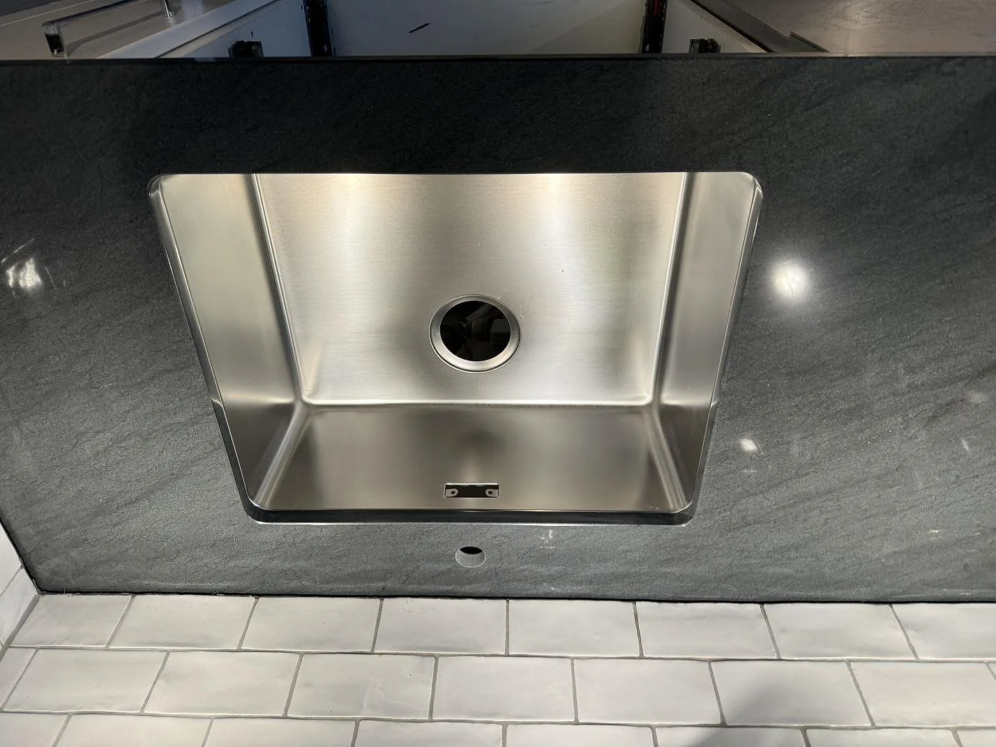 Detalj av rostfri diskho i mörk polerad Anthracite Elegante granit med vit kakelvägg i ett kök i Partille.
