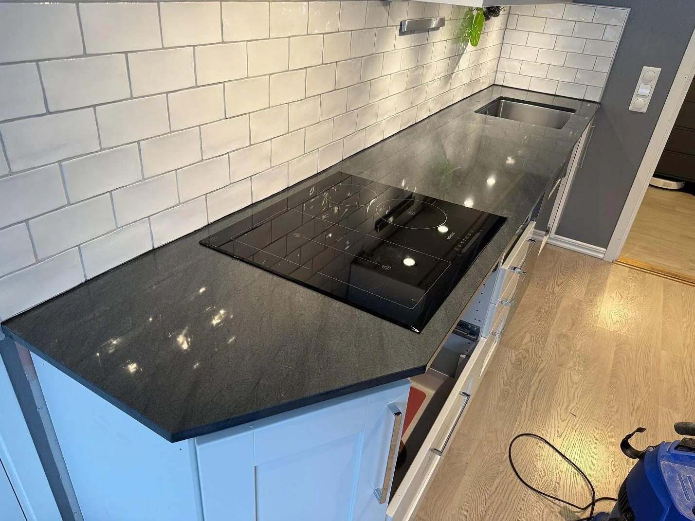 Köksbänkskiva i mörk polerad granit Anthracite Elegante med häll, rostfri diskho och vit kakelvägg i ett kök i Partille.