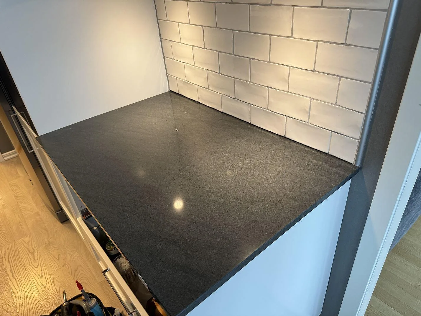 Rak bänkyta i polerad Anthracite Elegante granit mot vit kakelvägg och vita köksstommar i Partille.