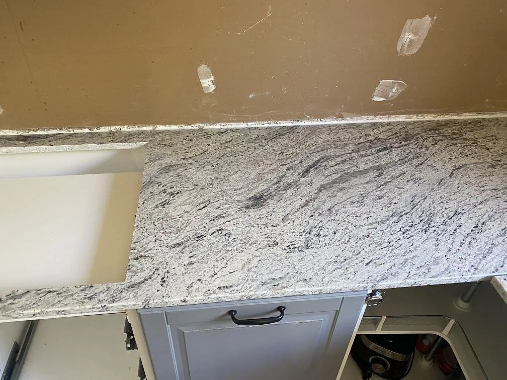 Polerad Antique White granit med tydlig grå ådring vid kökets arbetsyta och diskhoöppning i Älmhult.