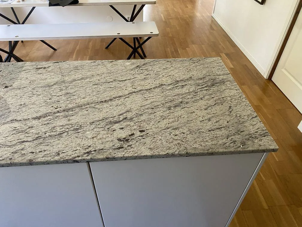 Bred arbetsyta i polerad Antique White granit över ljusa skåp i ett kök i Älmhult.