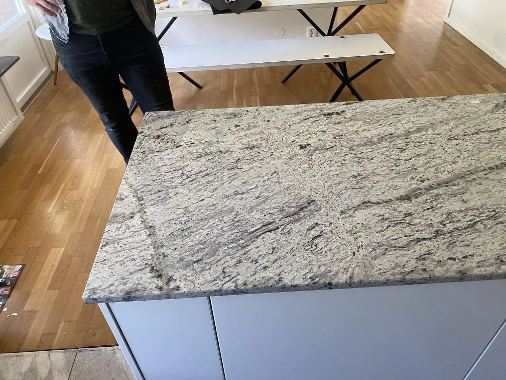 Detalj av polerad Antique White granit på köksyta med ljusa skåp och trägolv i Älmhult.