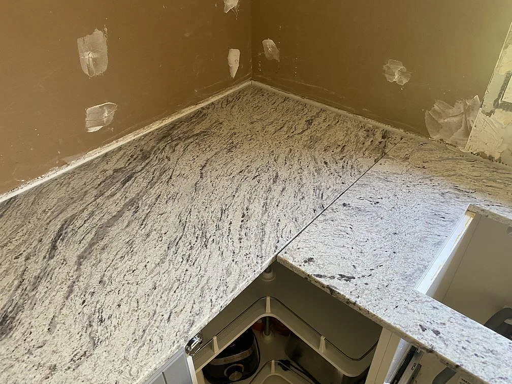 L-formad köksbänkskiva i polerad Antique White granit med öppning för diskho och synlig hörnsektion i Älmhult.