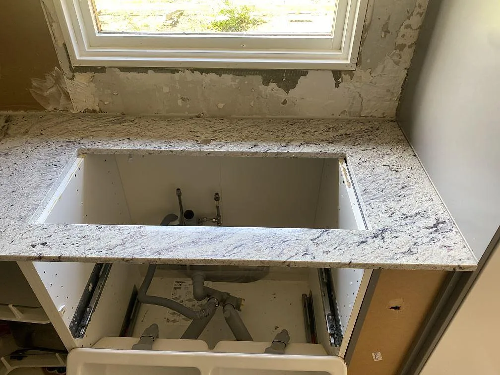 Köksbänkskiva i polerad Antique White granit med diskhoöppning, monterad på vita stommar under köksrenovering i Älmhult.