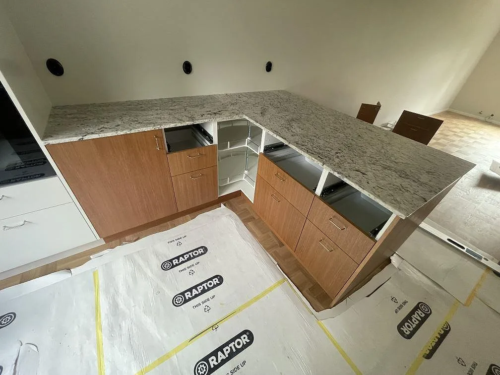 L-formad köksbänkskiva i polerad Antique White granit med ljus ådring på träinredning i Backvindeln.