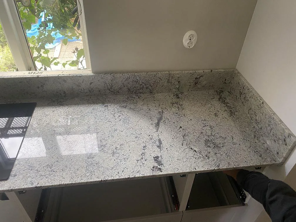 Antique White-granit köksbänkskiva vid fönstret med stänkkant och en induktionshäll under montering i ett kök i Borrby.