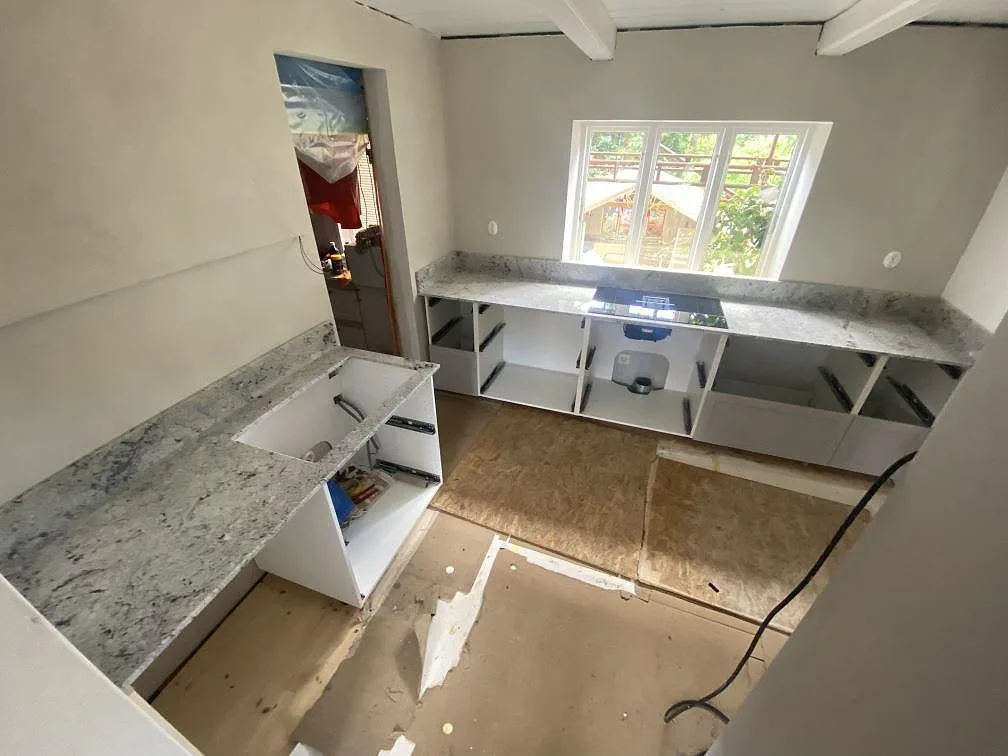 Köksbänkskiva i Antique White-granit, polerad, installerad i ett U-format kök under montering med köksö och induktionshäll vid fönstret i Borrby.