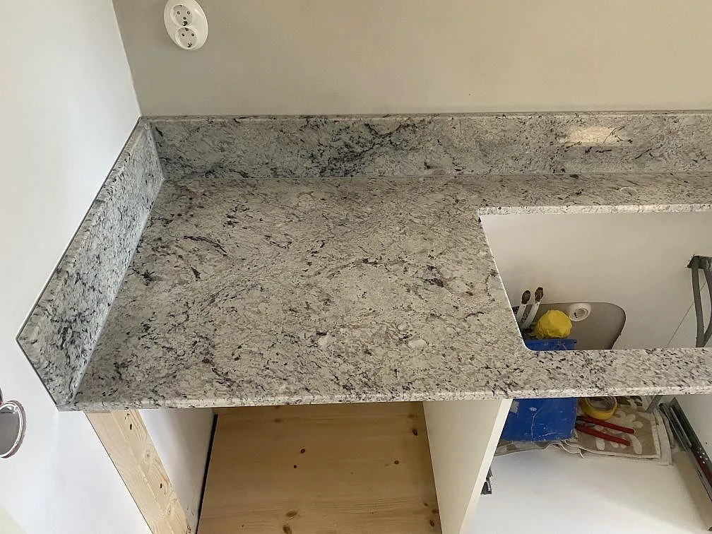 Polerad Antique White-granit som köksbänkskiva med uppvikt stänkkant och vägguttag längs väggen i ett kök i Borrby.