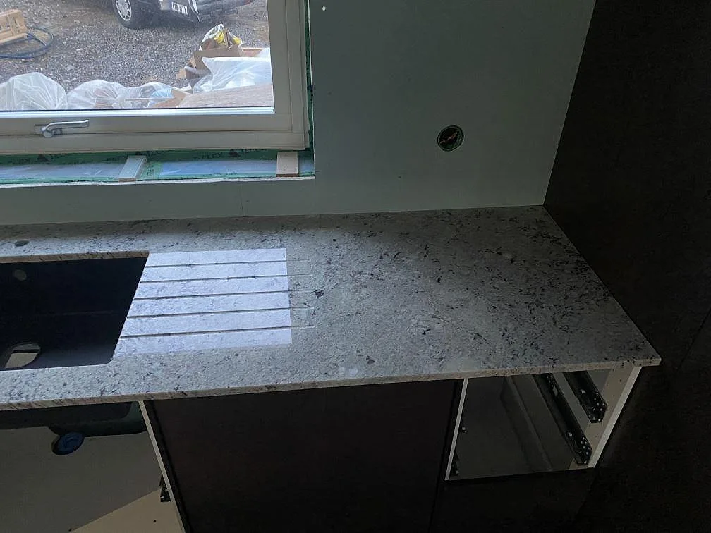 Antique White granit i polerad finish längs fönstervägg med mörk träinredning i ett kök i Falkenberg.