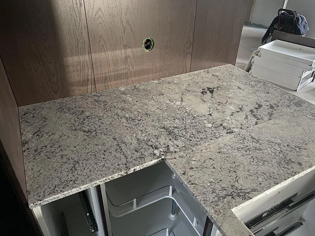 Köksbänkskiva i polerad Antique White granit med livlig ådring och vinklad montering i ett kök i Falkenberg.