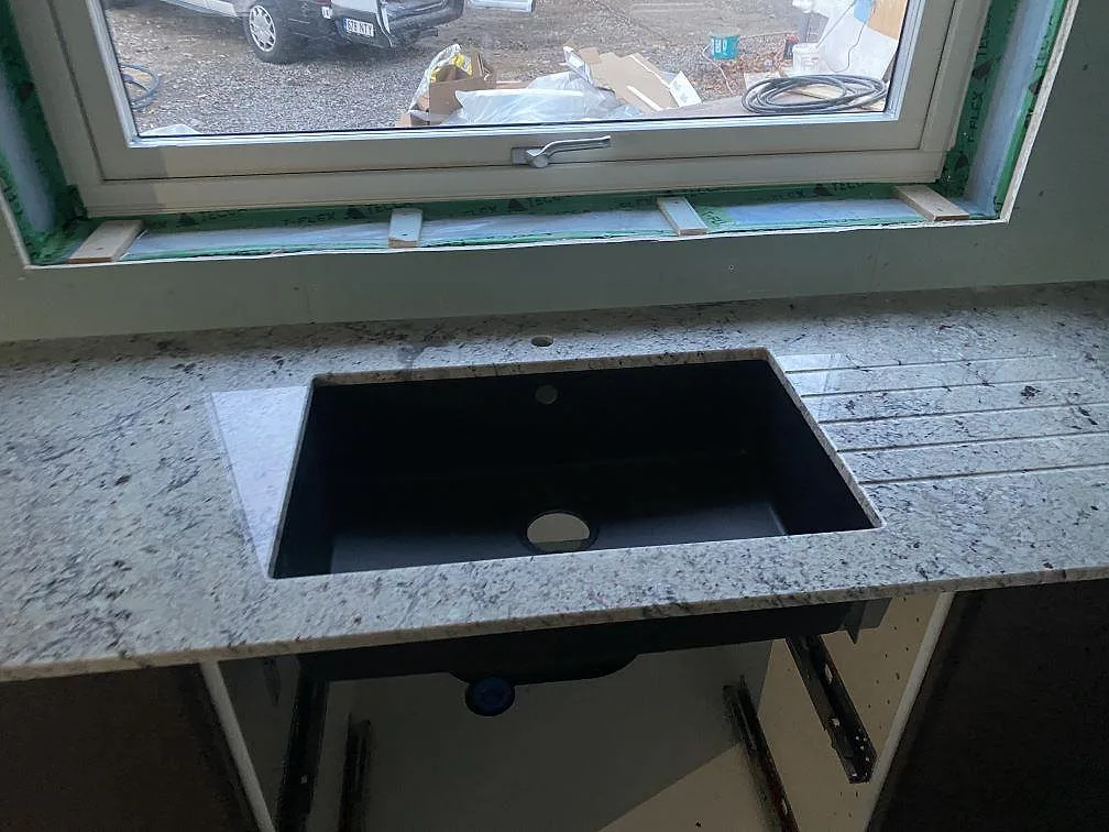 Polerad Antique White granit runt en svart diskho vid fönster i ett kök under montering i Falkenberg.