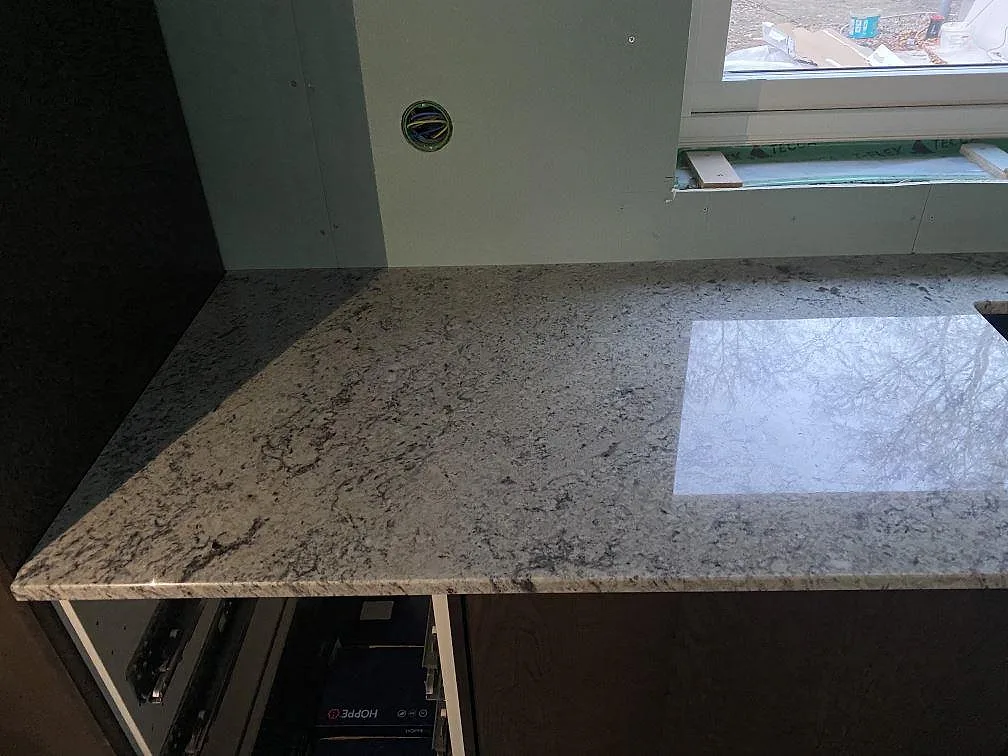 Närbild på köksbänkskiva i Antique White granit med ljus och grå ådring, polerad yta, i ett kök i Falkenberg.