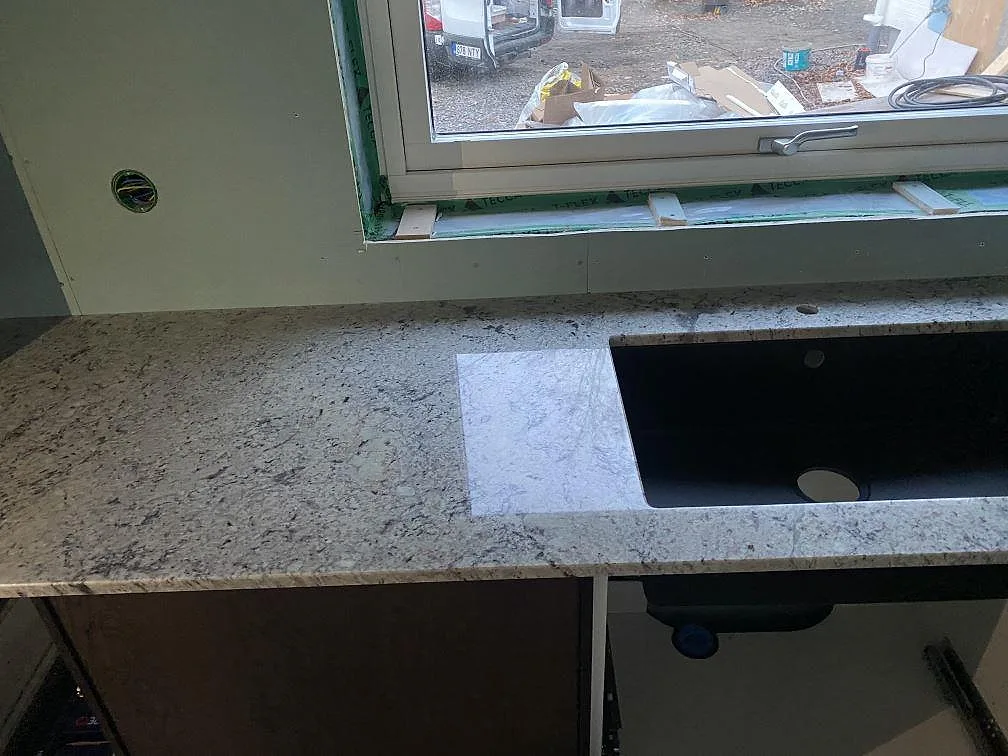 Köksbänkskiva i vit-grå Antique White granit med underlimmad svart diskho, mitt under montering i Falkenberg