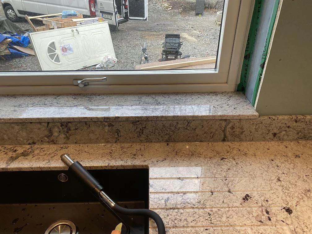 Bänkskiva i Antique White granit vid fönster med urtag för underlimmad diskho i ett kök i Falkenberg.