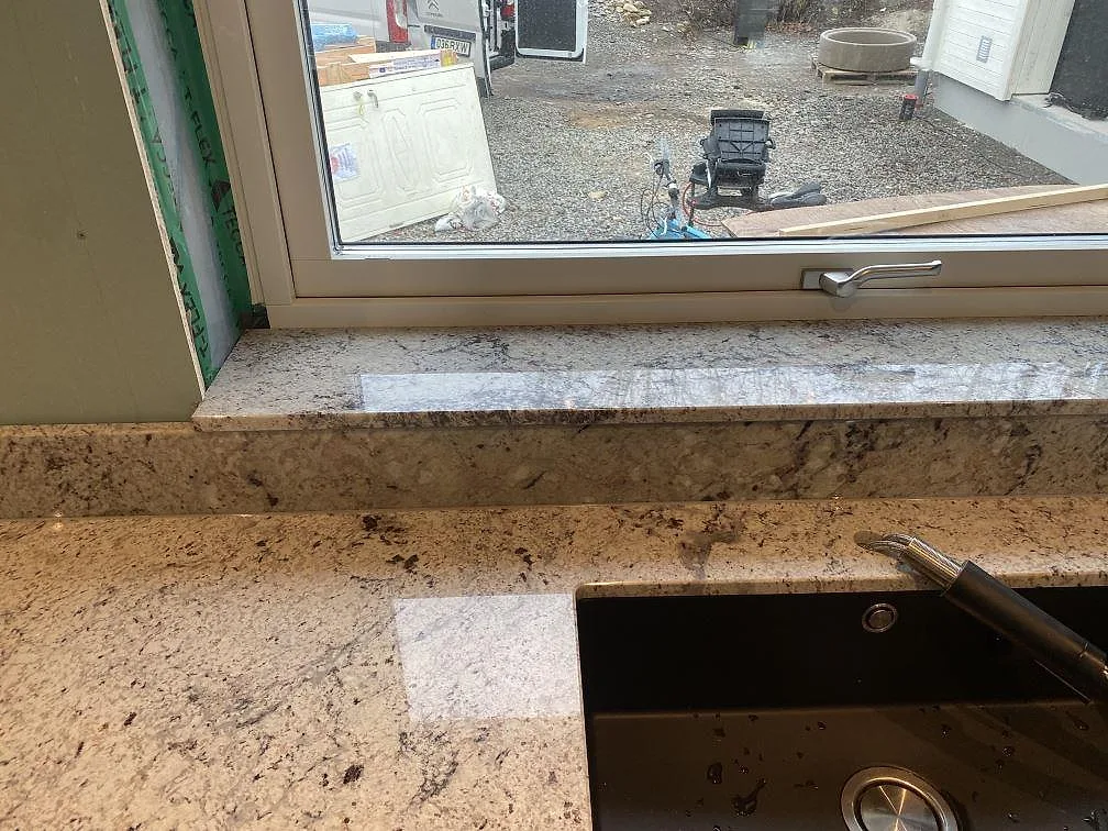 Polerad Antique White granitbänkskiva med diskhourtag och blandarfäste vid fönstret i ett kök i Falkenberg.