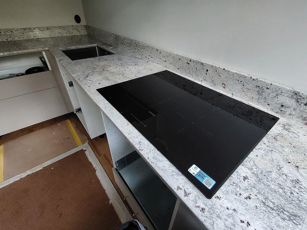 Köksbänkskiva i polerad Antique White granit med svart häll och uppvikt stänkkant i ett kök i Farsta.