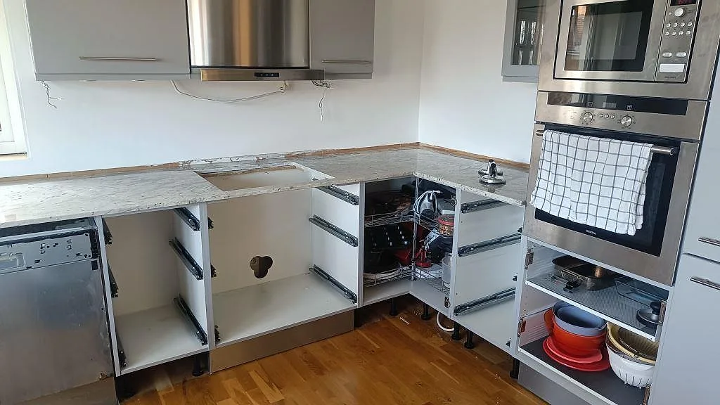 L-formad köksbänk i polerad Antique White-granit med stänkkant, köksfläkt och inbyggda ugnar i ett kök i Frillesås.