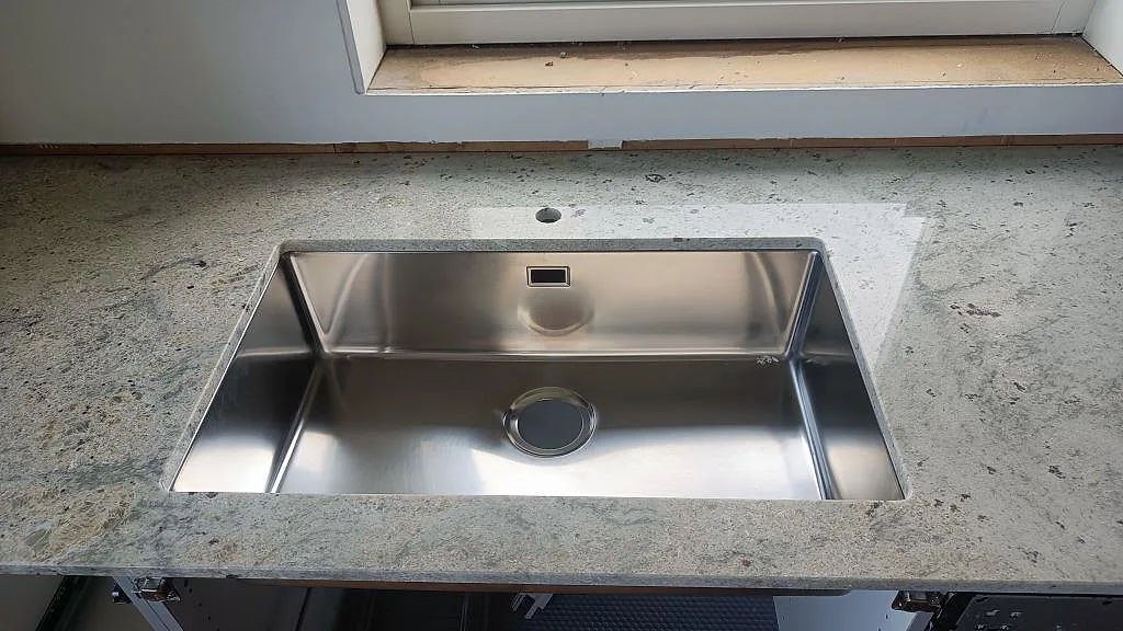 Underlimmad rostfri diskho infälld i köksbänkskiva av polerad Antique White-granit i Frillesås.