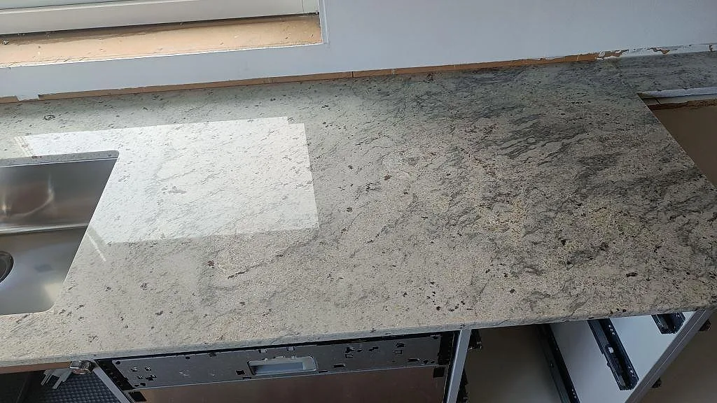 Köksbänk i polerad Antique White-granit sedd ovanifrån med rostfri diskho och tydlig ådring i grått och vinrött, Frillesås.