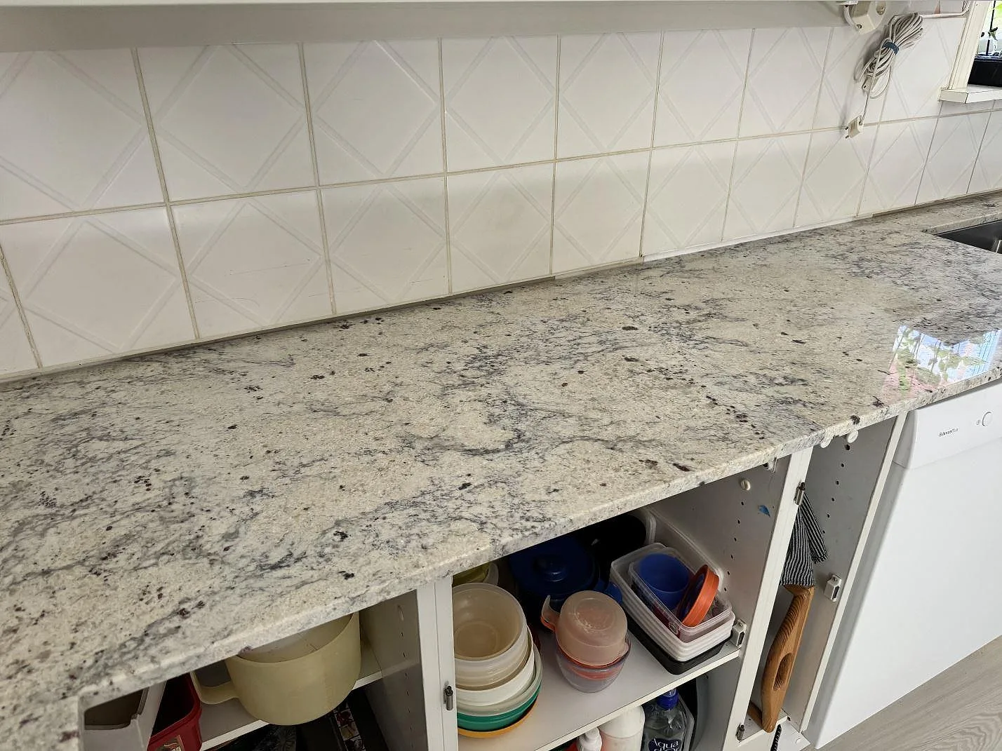 Polerad Antique White granit som köksbänkskiva längs vit kakelvägg och öppna stommar i Gärds Köpinge.