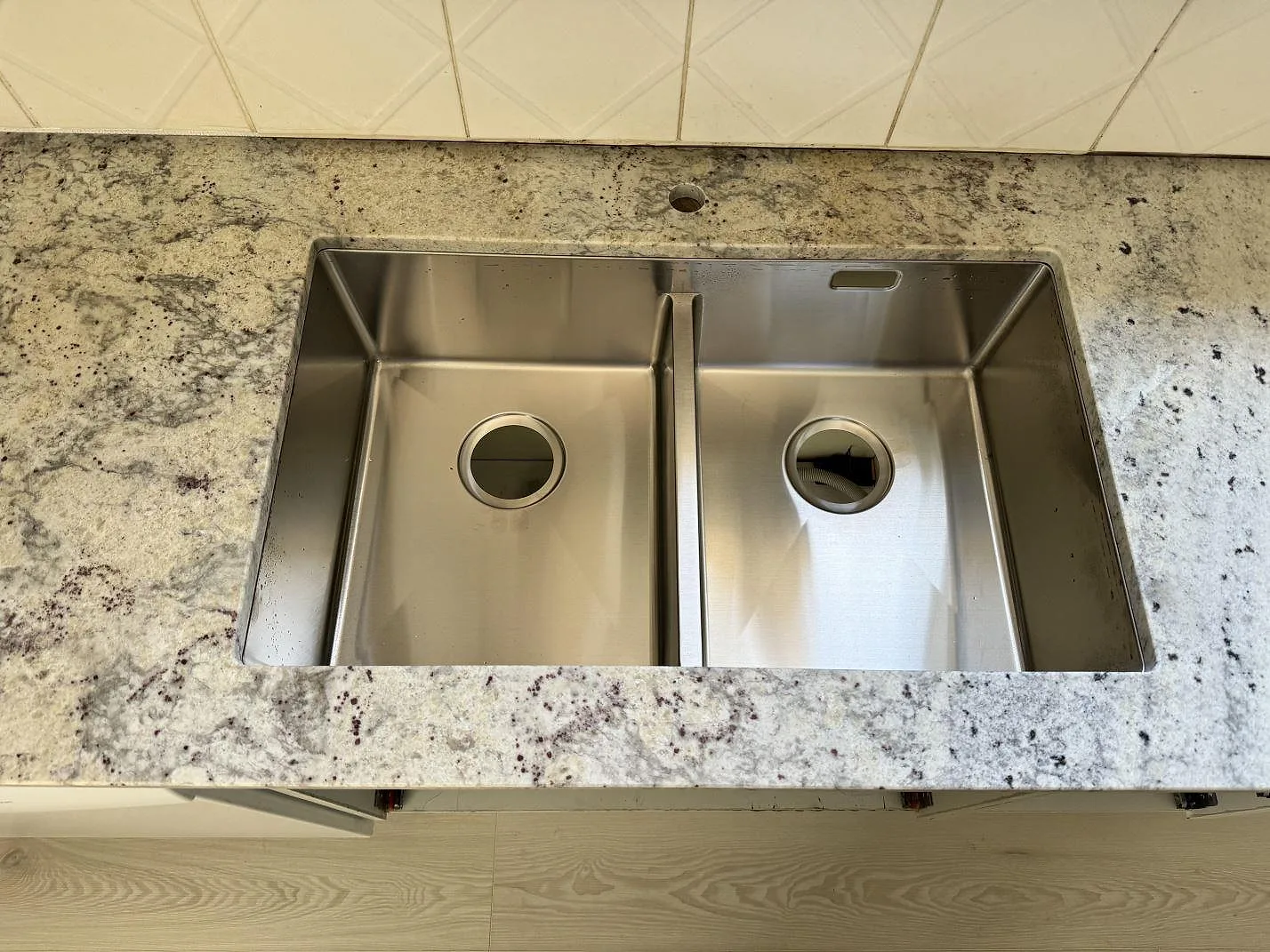 Närbild på underlimmad dubbel rostfri diskho i polerad Antique White granit i kök i Gärds Köpinge.