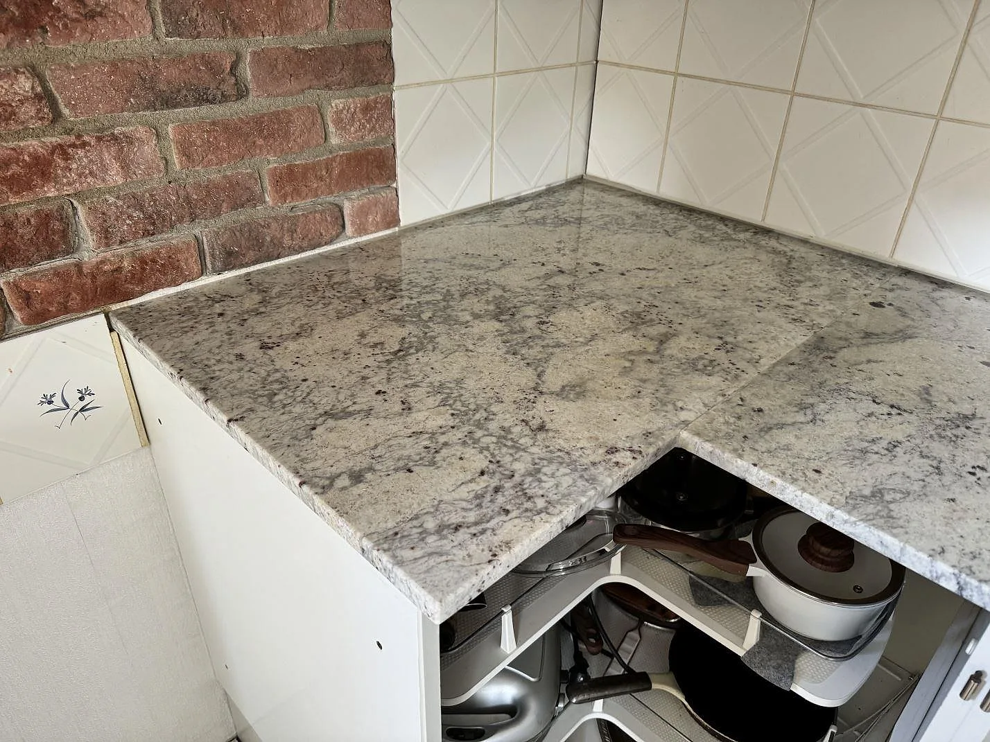 Hörn av köksbänkskiva i Antique White granit mot tegel och vitt kakel i Gärds Köpinge.