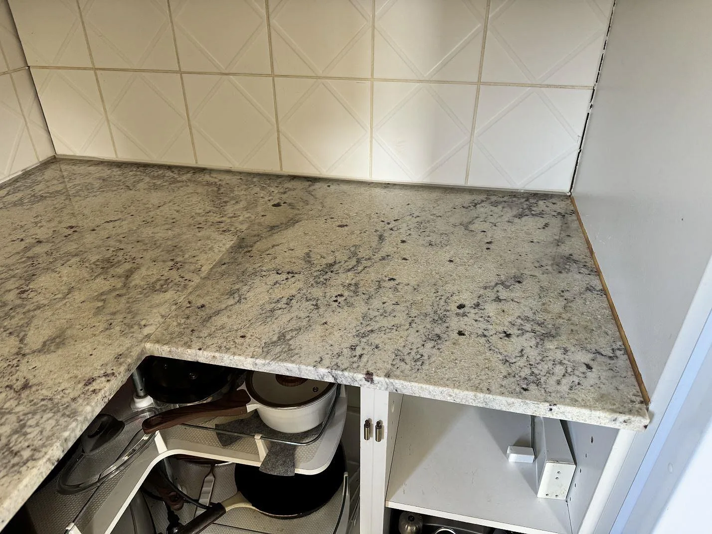 Sidoyta av köksbänkskiva i polerad Antique White granit vid vitt kakel i Gärds Köpinge.