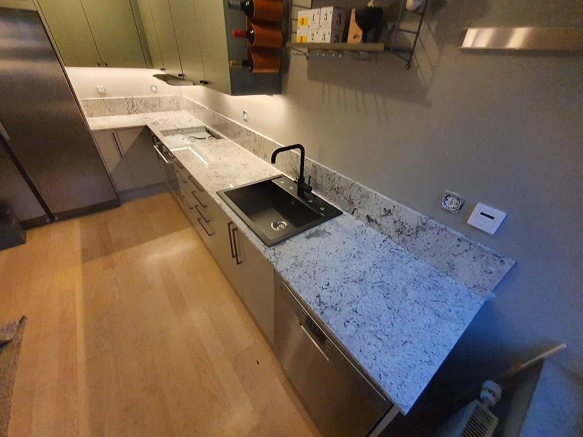 Köksbänkskiva i Antique White granit, polerad, med svart nedfälld diskho och svart blandare i ett L format kök i Gustavsberg.