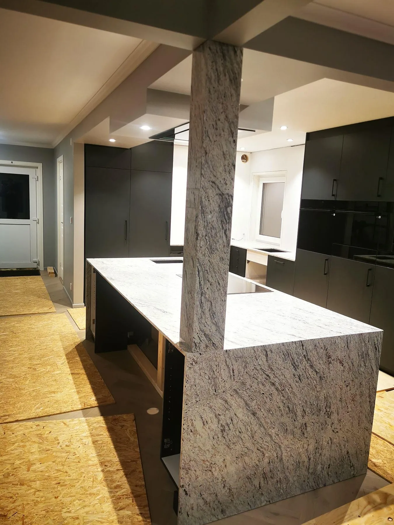Köksbänkskiva och köksö i Antique White granit, polerad, med induktionshäll och mörka köksluckor i ett kök i Hässelby.
