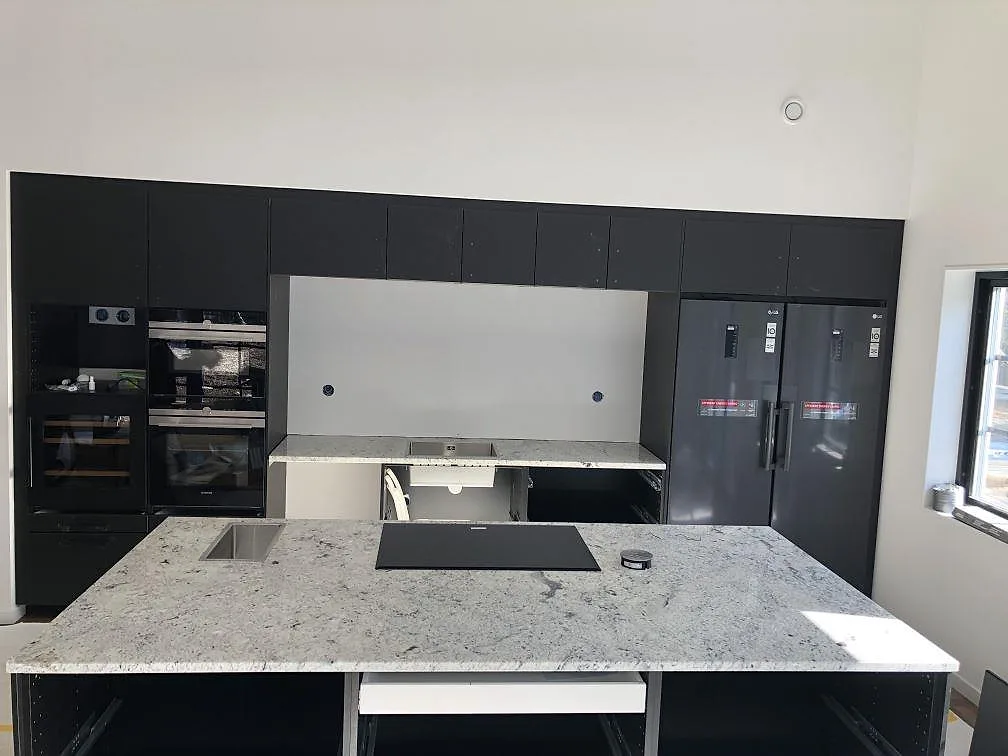 Närbild på kanten av en polerad köksbänkskiva i vit spräcklig Antique White granit i ett kök under montering i Hindås.