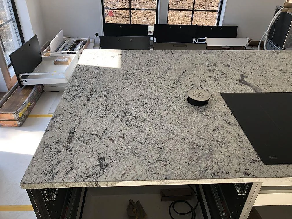 Polerad köksbänkskiva i vit Antique White granit med underlimmad rostfri diskho längs väggen i ett kök i Hindås.