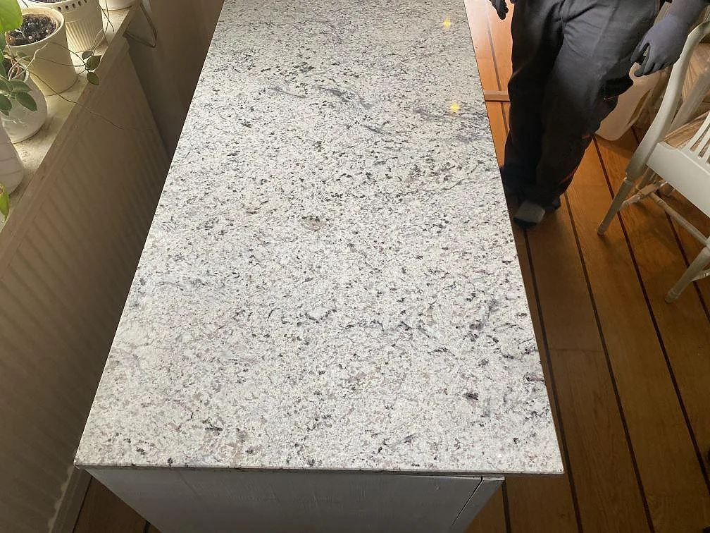 Bänkskiva i Antique White granit, polerad, på en vit stomme i ett rum med trägolv i Hökerum.