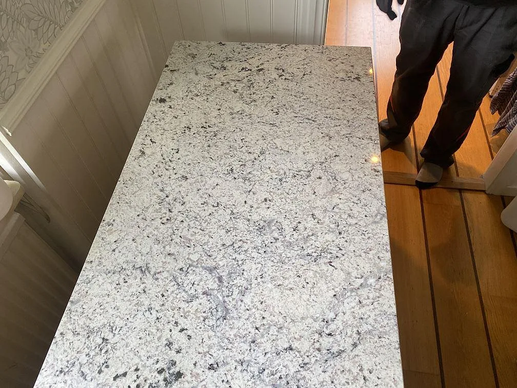 Närbild av polerad Antique White granit på en rektangulär bänkskiva vid vägg och trägolv i Hökerum.