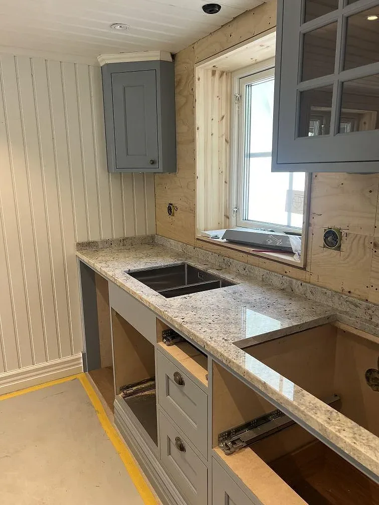 Köksbänkskiva i polerad Antique White-granit med stänkkant, grå luckor och fönsterläge i Hökerum.