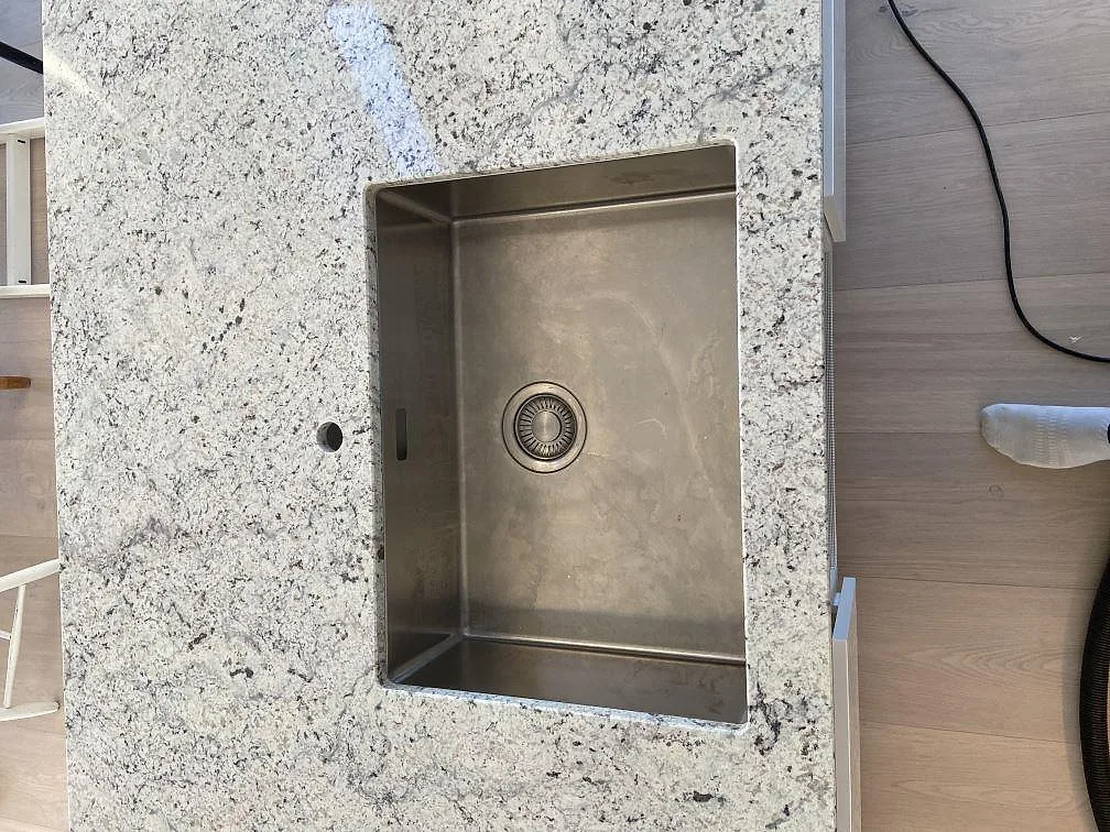 Närbild på undermonterad rostfri diskho i polerad Antique White granitbänkskiva i ett kök i Höllviken.