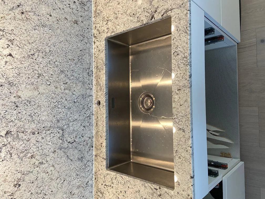 Underlimmad rostfri diskho infälld i polerad Antique White granitbänkskiva i ett kök i Höllviken.