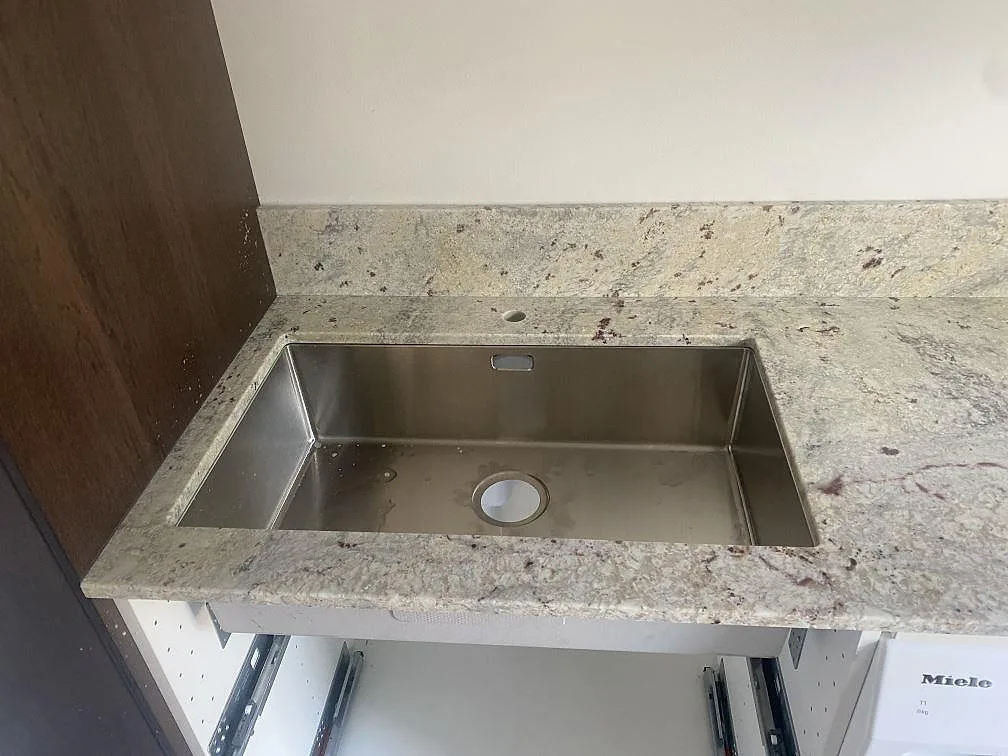 Närbild på polerad Antique White granit med rostfri diskho ovanpå stenen och stänkkant i Höllviken.