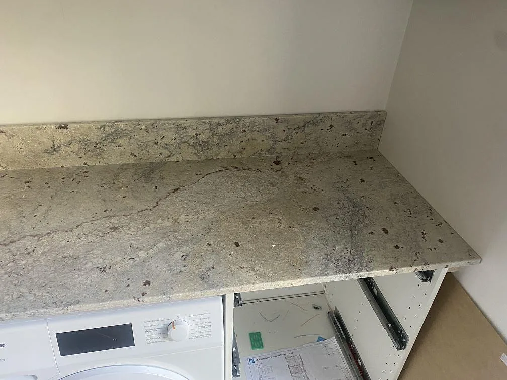 Polerad Antique White granit med krämig ådring och uppvikt stänkkant som arbetsbänk i tvättstuga i Höllviken.