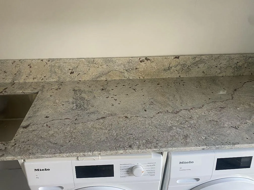 Ytdetalj av polerad Antique White granit över Miele-tvättmaskiner med diskho och stänkkant i Höllviken.