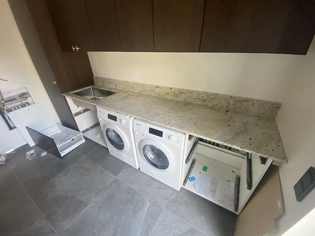 Bänkskiva i polerad Antique White granit med rostfri diskho och uppvikt stänkkant i en tvättstuga i Höllviken.