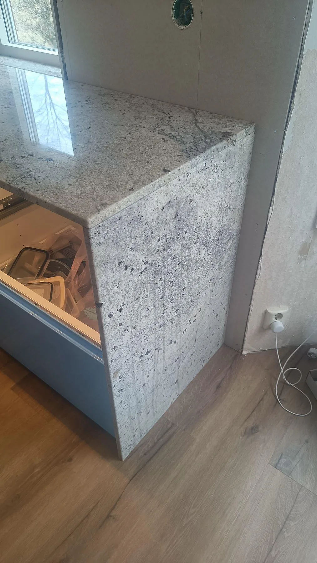 Neddragen sidogavel och bänkskiva i polerad Antique White-granit vid halvö i ett kök i Hörby.