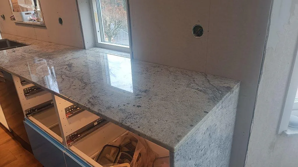 Polerad Antique White-granit i kök i Hörby med neddragen sidogavel vid halvön och bänkskiva under fönster.