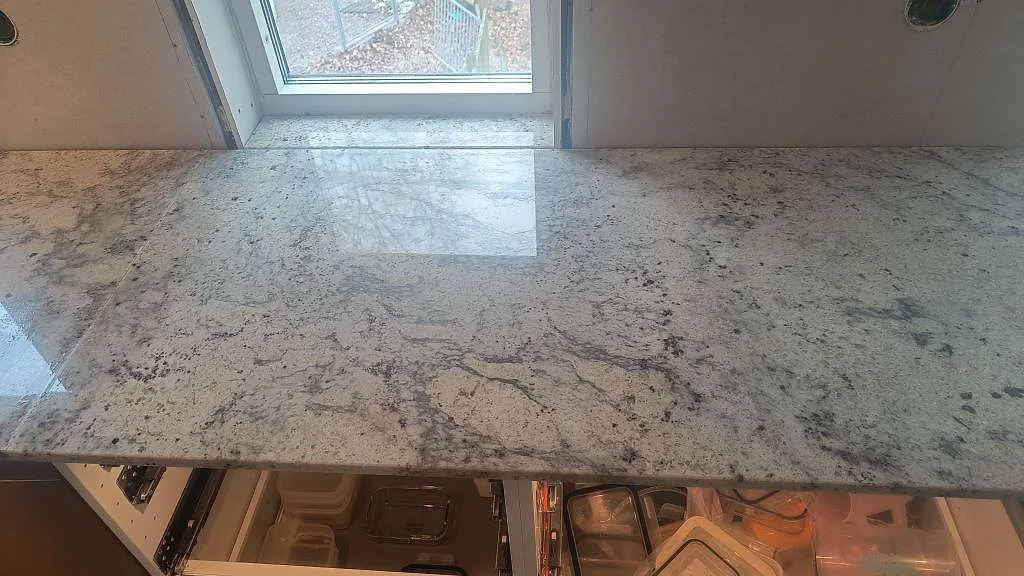 Närbild på polerad Antique White-granit med grå ådring framför fönster i ett kök i Hörby.