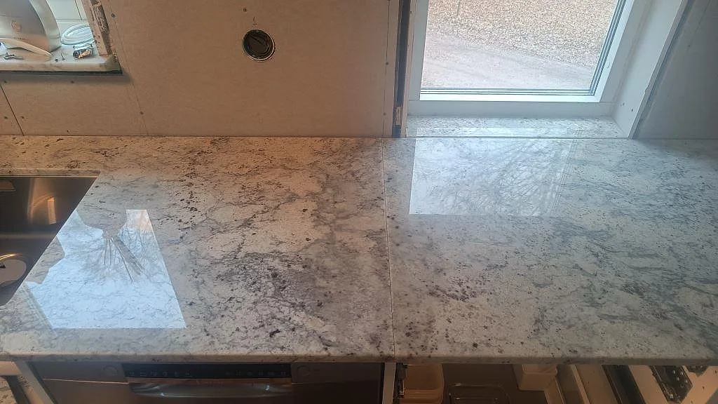 Lång köksbänkskiva i polerad Antique White-granit med fönsterreflektion och synlig skarv i Hörby.