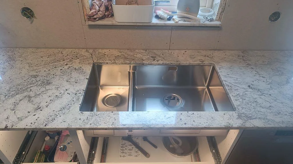 Rostfri underlimmad diskho i polerad Antique White-granit med ljus ådring i ett kök i Hörby.