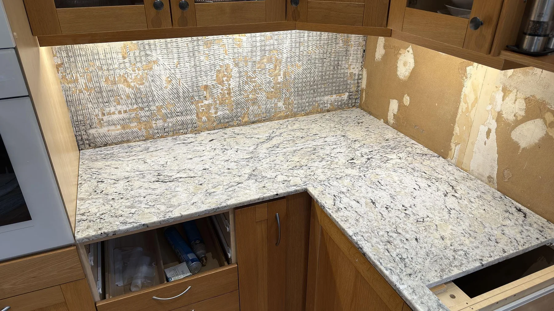 Hörnsektion av polerad Antique White granit i kök i Huddinge, med ljus ådring och bänkskiva monterad mot träinredning.