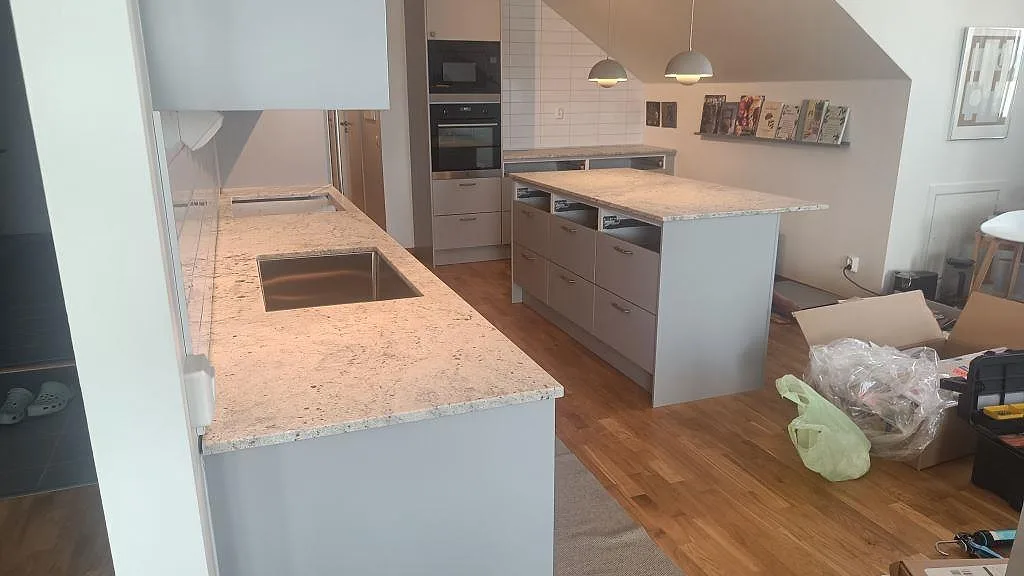 Köksbänkskivor och köksö i matt Antique White granit med underlimmad rostfri diskho och öppna köksstommar under montering i Jönköping.