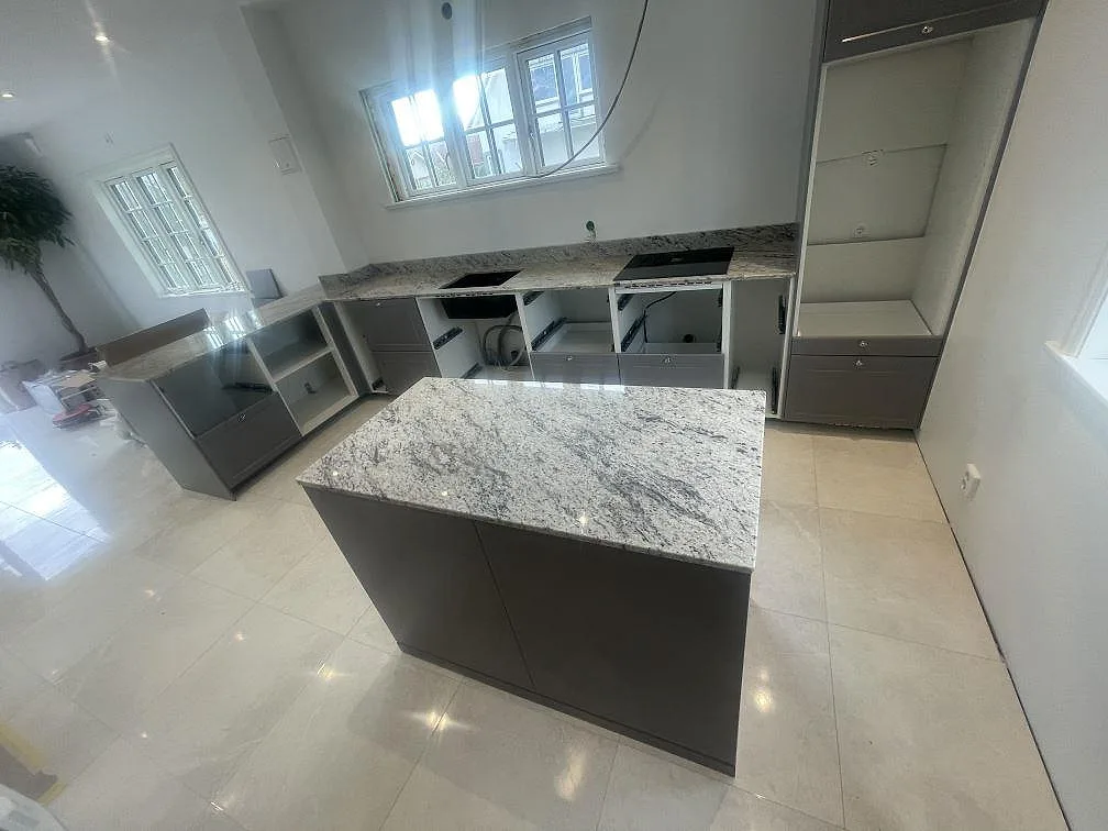 Köksbänkskiva i polerad Antique White granit med halvö, svart häll och svart diskho i ett kök i Klippan.